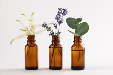 Photo of Essential oils with different plants in bottles on light grey background