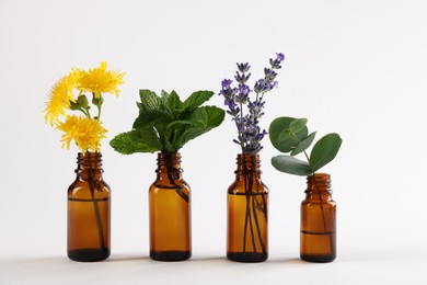 Photo of Essential oils with different plants in bottles on light grey background
