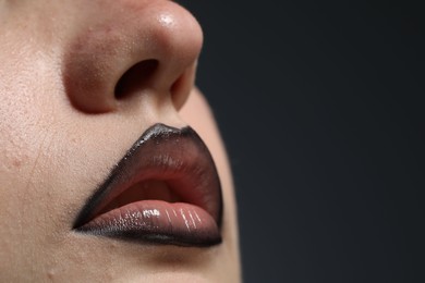 Photo of Beautiful young woman with black lip liner on dark grey background, closeup. Space for text