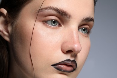 Photo of Beautiful young woman with black lip liner on light grey background, closeup