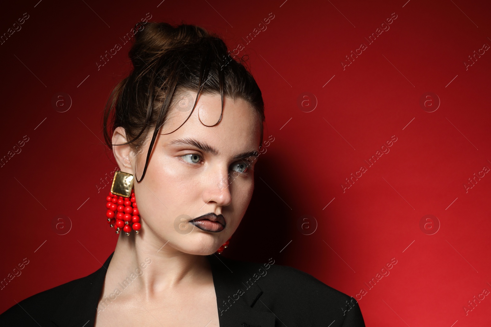 Beautiful young woman with black lip liner wearing stylish earrings on dark red background, space for text Photo of Beautiful young woman with black lip liner wearing stylish earrings on dark red background, space for text