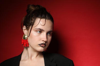 Photo of Beautiful young woman with black lip liner wearing stylish earrings on dark red background, space for text