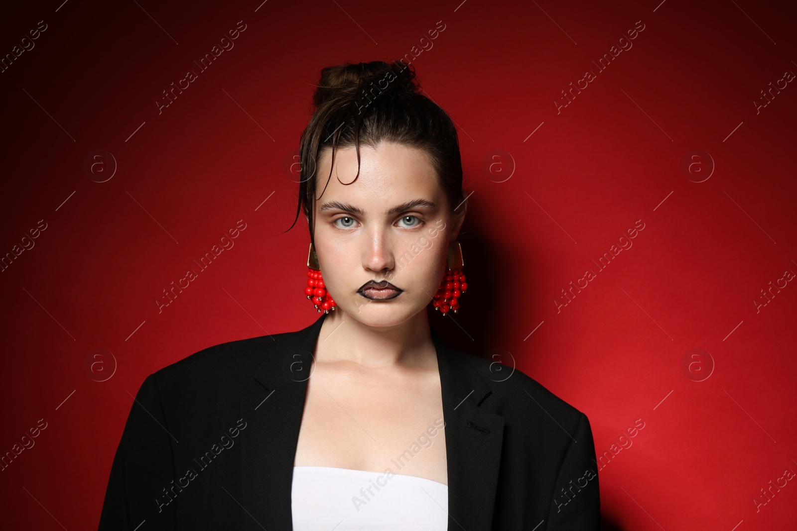 Beautiful young woman with black lip liner wearing stylish earrings on dark red background Photo of Beautiful young woman with black lip liner wearing stylish earrings on dark red background