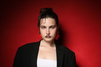 Photo of Beautiful young woman with black lip liner wearing stylish earrings on dark red background