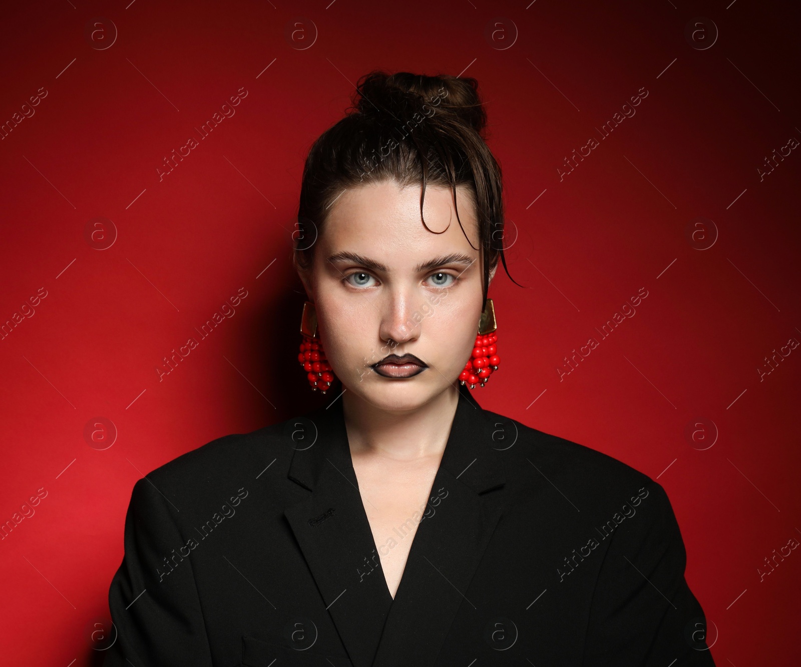 Beautiful young woman with black lip liner wearing stylish earrings on dark red background Photo of Beautiful young woman with black lip liner wearing stylish earrings on dark red background
