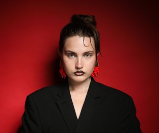 Photo of Beautiful young woman with black lip liner wearing stylish earrings on dark red background