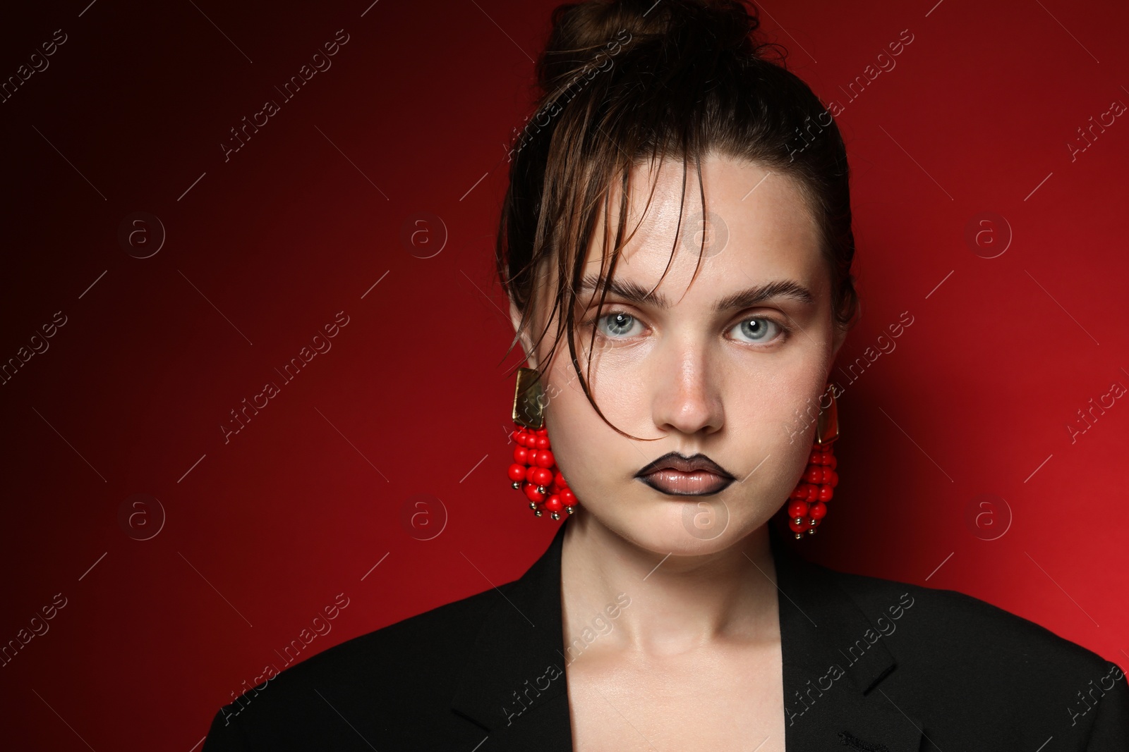 Beautiful young woman with black lip liner wearing stylish earrings on dark red background, space for text Photo of Beautiful young woman with black lip liner wearing stylish earrings on dark red background, space for text