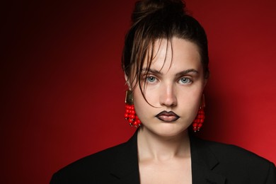 Photo of Beautiful young woman with black lip liner wearing stylish earrings on dark red background, space for text
