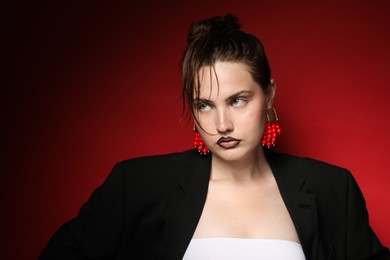 Photo of Beautiful young woman with black lip liner wearing stylish earrings on dark red background, space for text