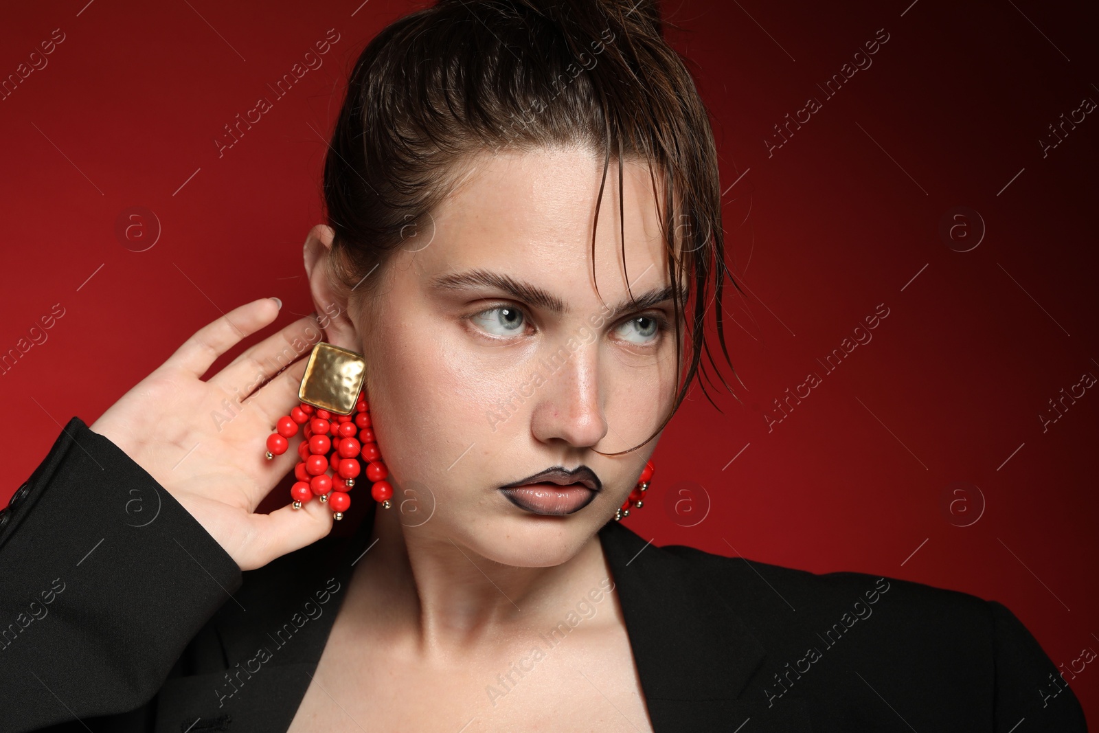 Beautiful young woman with black lip liner wearing stylish earrings on dark red background Photo of Beautiful young woman with black lip liner wearing stylish earrings on dark red background