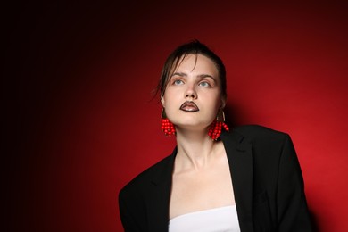 Photo of Beautiful young woman with black lip liner wearing stylish earrings on dark red background