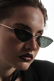 Photo of Beautiful young woman with black lip liner wearing wet sunglasses on white background, closeup