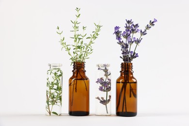 Photo of Essential oils with different plants in bottles on light grey background