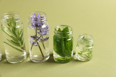 Photo of Essential oils with different plants in bottles on green background, closeup