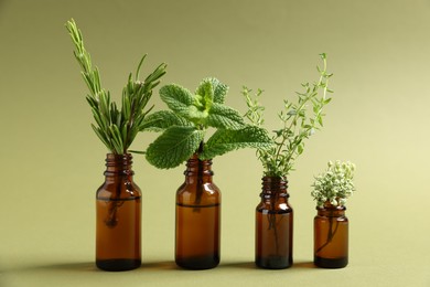 Photo of Essential oils with different plants in bottles on green background