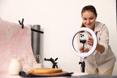 Photo of Woman taking picture of tasty pie and milk in studio, selective focus. Professional food photography