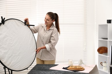 Photo of Woman using reflector to take picture of tasty pie and milk in studio. Professional food photography