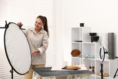 Photo of Woman using reflector to take picture of tasty pie and milk in studio. Professional food photography