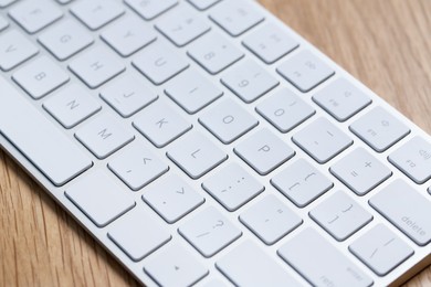 Photo of Modern white wireless keyboard on wooden table, closeup