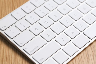 Photo of Modern white wireless keyboard on wooden table, closeup