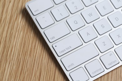 Photo of Modern white wireless keyboard on wooden table, closeup. Space for text