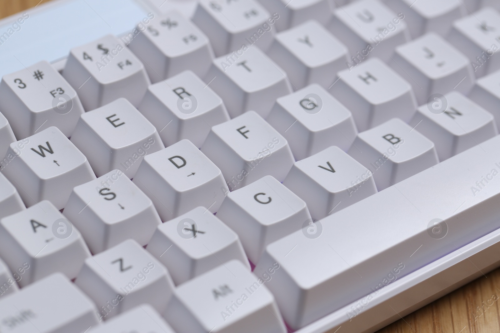 Modern white keyboard with RGB lighting on wooden table, closeup Photo of Modern white keyboard with RGB lighting on wooden table, closeup