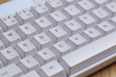 Photo of Modern white keyboard with RGB lighting on wooden table, closeup
