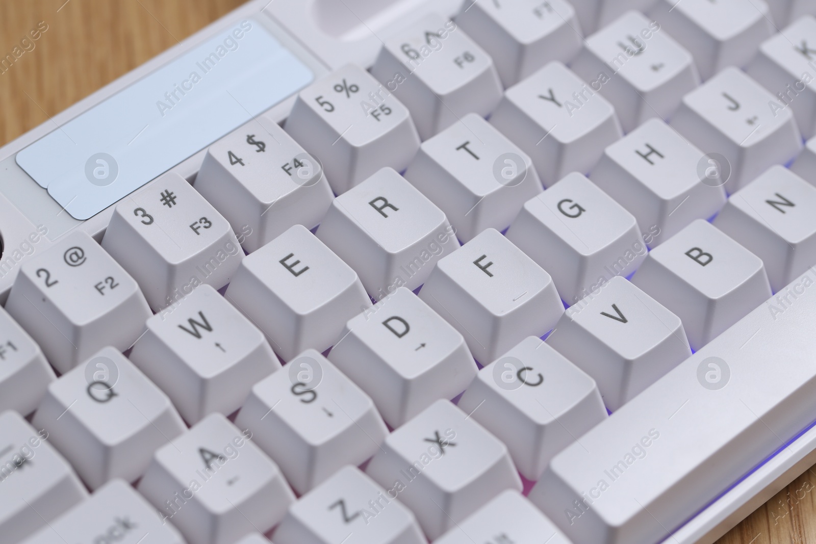 Modern white keyboard with RGB lighting on wooden table, closeup Photo of Modern white keyboard with RGB lighting on wooden table, closeup