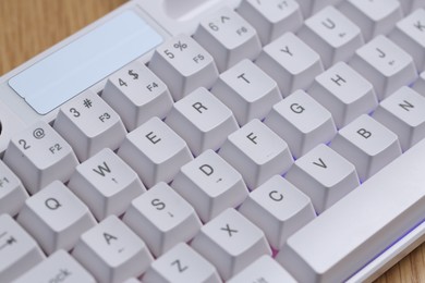 Photo of Modern white keyboard with RGB lighting on wooden table, closeup
