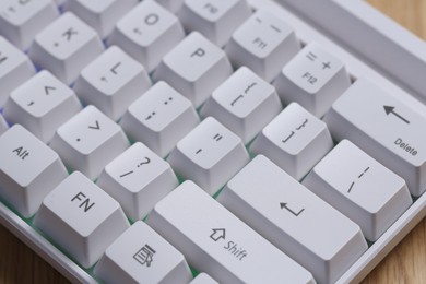 Photo of Modern white keyboard with RGB lighting on wooden table, closeup