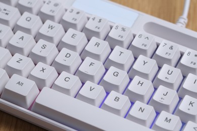 Photo of Modern white keyboard with RGB lighting on wooden table, closeup