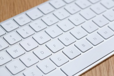 Photo of Modern white wireless keyboard on wooden table, closeup