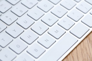 Photo of Modern white wireless keyboard on wooden table, closeup