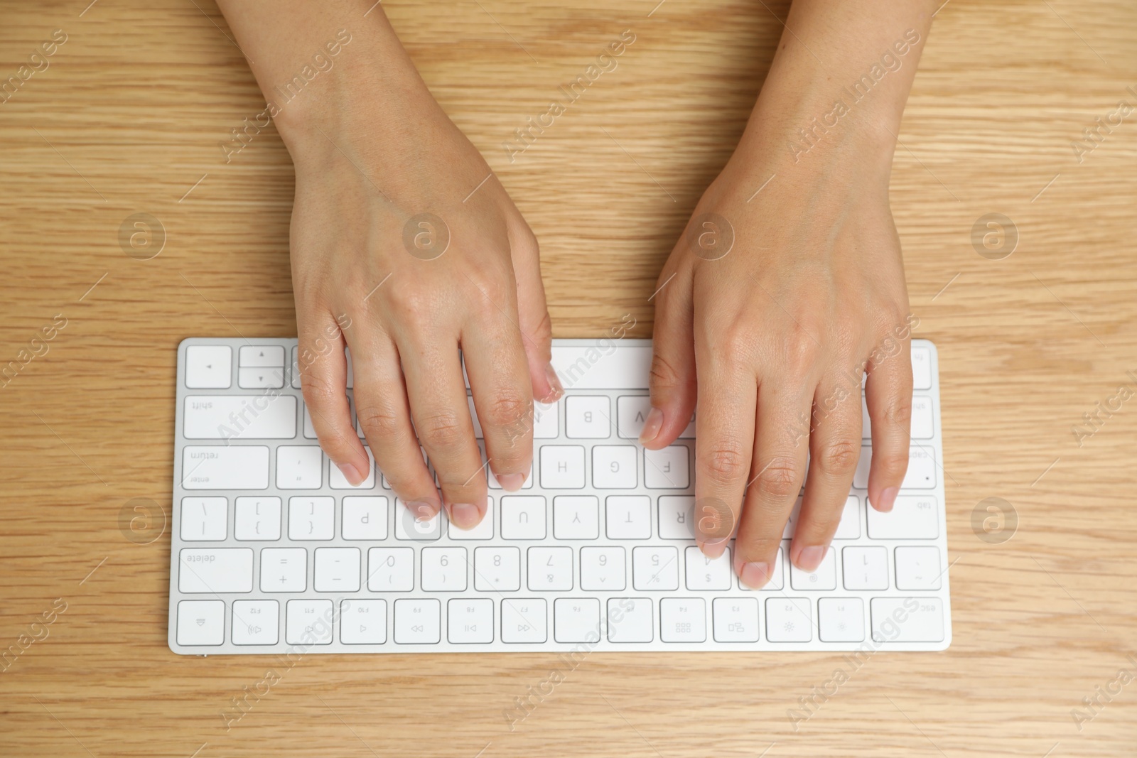 Woman typing on white wireless keyboard at wooden table, top view Photo of Woman typing on white wireless keyboard at wooden table, top view