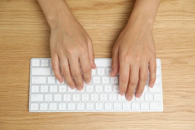 Photo of Woman typing on white wireless keyboard at wooden table, top view