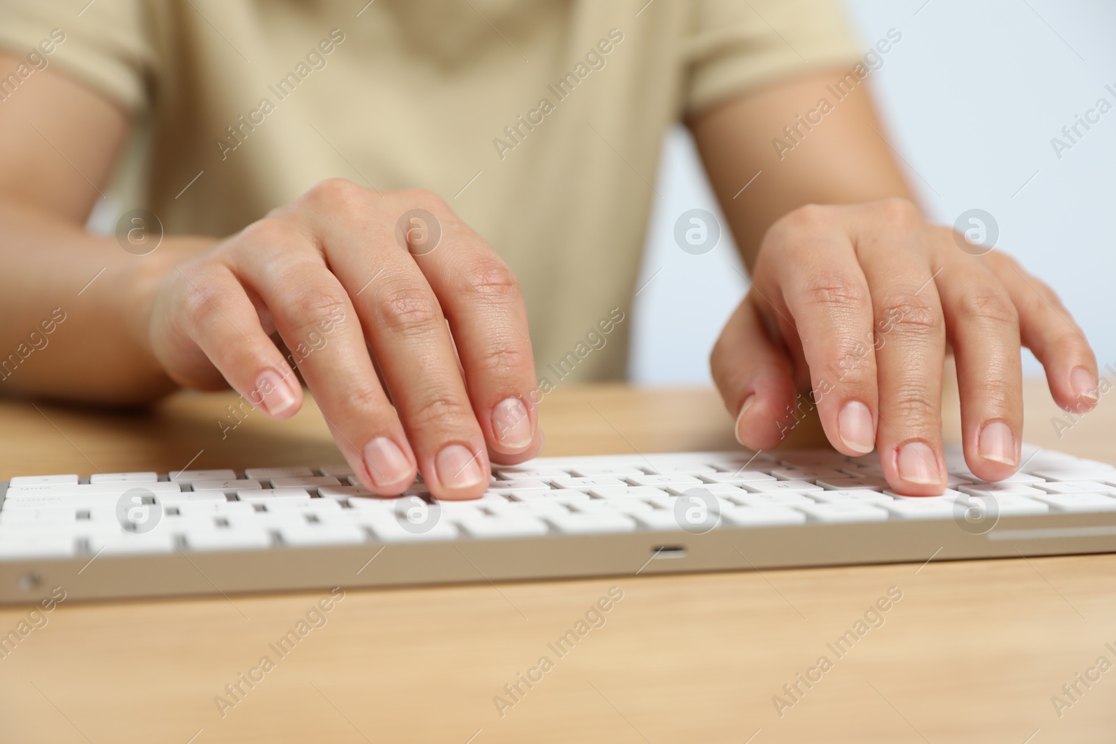 Woman typing on white wireless keyboard at wooden table, closeup Photo of Woman typing on white wireless keyboard at wooden table, closeup