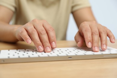 Photo of Woman typing on white wireless keyboard at wooden table, closeup