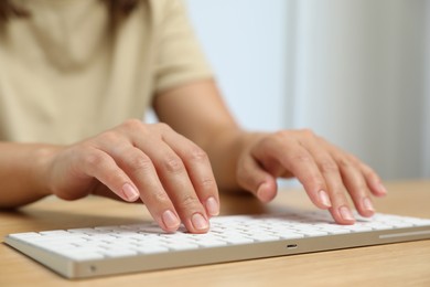 Photo of Woman typing on white wireless keyboard at wooden table, closeup