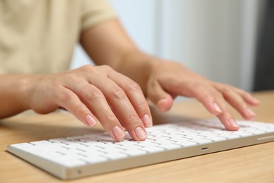 Photo of Woman typing on white wireless keyboard at wooden table, closeup