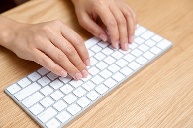 Photo of Woman typing on white wireless keyboard at wooden table, closeup