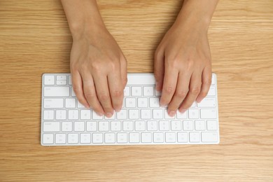 Photo of Woman typing on white wireless keyboard at wooden table, top view