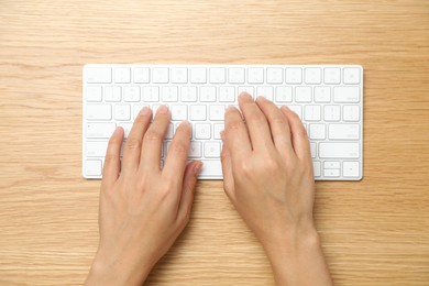 Photo of Woman typing on white wireless keyboard at wooden table, top view