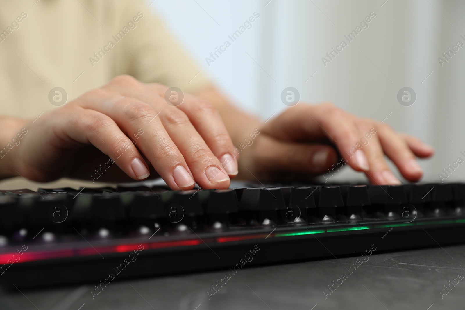 Woman typing on black keyboard with RGB lighting at grey table, closeup Photo of Woman typing on black keyboard with RGB lighting at grey table, closeup