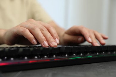 Photo of Woman typing on black keyboard with RGB lighting at grey table, closeup