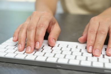 Photo of Woman typing on white wireless keyboard at grey table, closeup