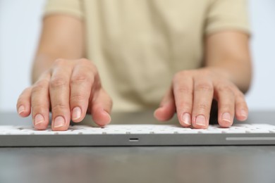 Photo of Woman typing on white wireless keyboard at grey table, closeup