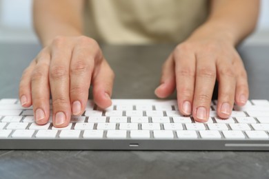 Photo of Woman typing on white wireless keyboard at grey table, closeup