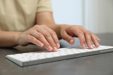 Photo of Woman typing on white wireless keyboard at grey table, closeup