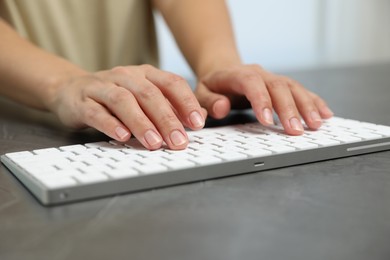 Photo of Woman typing on white wireless keyboard at grey table, closeup
