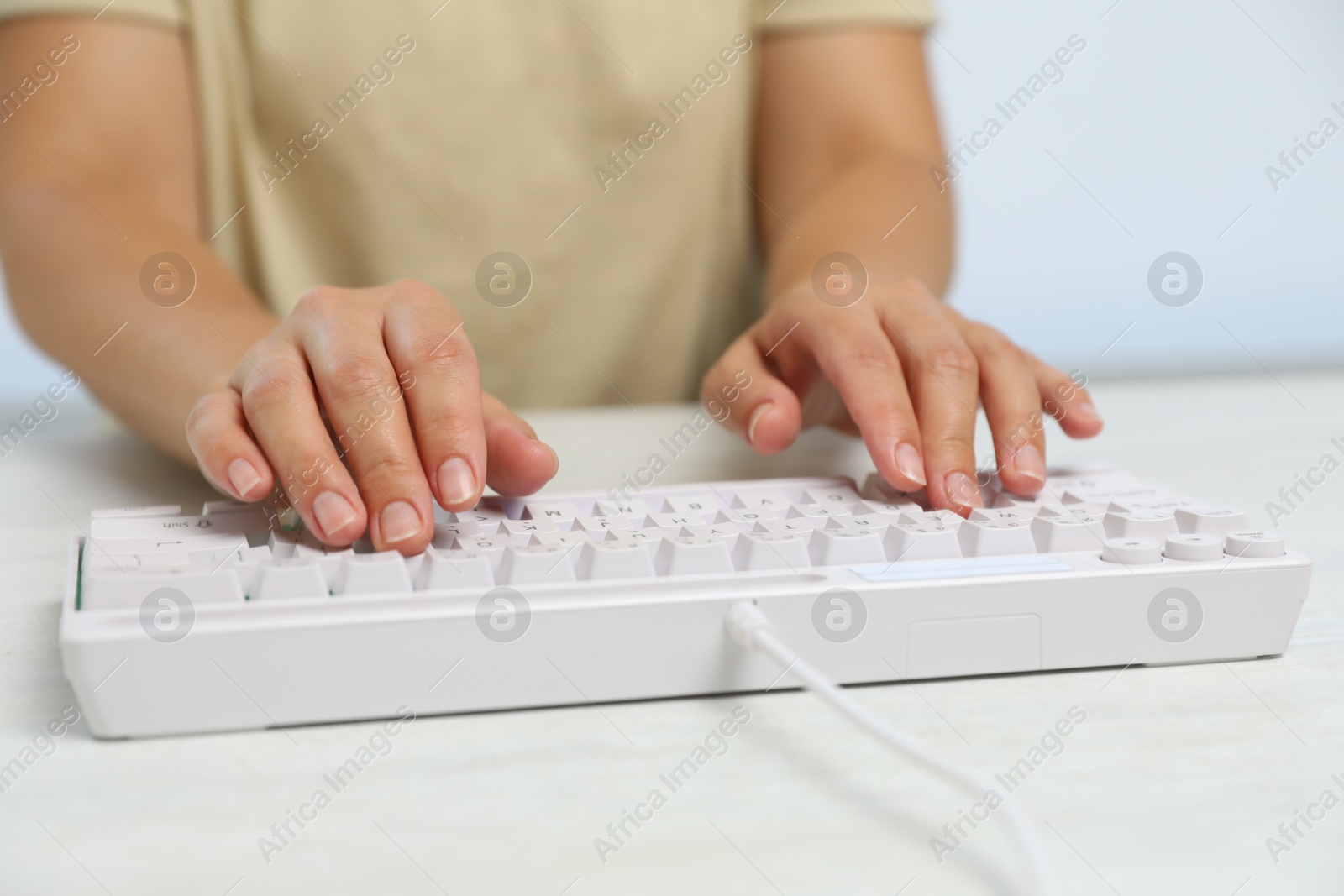 Woman typing on modern keyboard with RGB lighting at white wooden table, closeup Photo of Woman typing on modern keyboard with RGB lighting at white wooden table, closeup